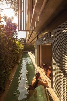 two women in swimsuits sitting on the edge of a swimming pool next to a building