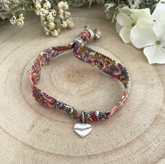 a bracelet with a heart charm on it next to some flowers and a white flower