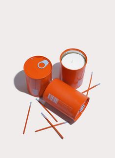 an orange cup and some sticks on a white surface with one candle in the middle