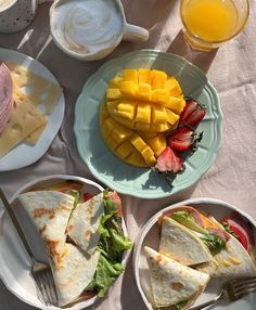 plates with sandwiches and fruit on them sitting on a table next to glasses of orange juice