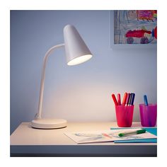 a desk lamp sitting on top of a table next to some pens and pencils