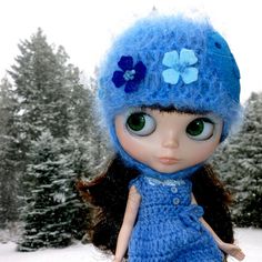 a doll wearing a blue hat and dress in the snow