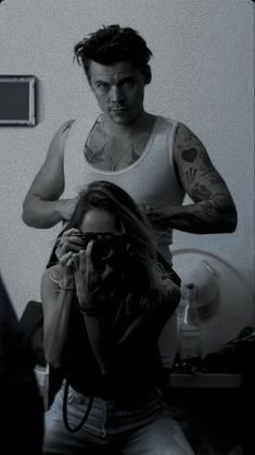 a man standing next to a woman in a room with tattoos on his arms and shoulder