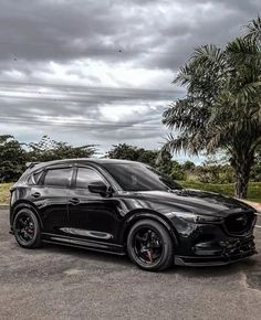 a black mazda car parked in a parking lot next to a palm tree and cloudy sky