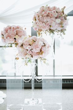 two clear vases filled with pink flowers sitting on top of a table next to a window