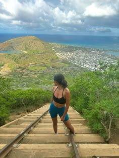 a woman standing on top of a train track next to the ocean and hills in the background