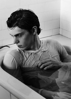 a man sitting in a bathtub with his hands on his chest and looking off into the distance