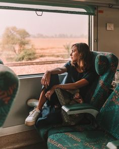 a woman sitting on a train seat looking out the window with her legs propped up