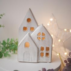 there is a small white house on top of a cake stand next to some flowers