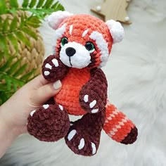 a hand holding a small crocheted red panda bear