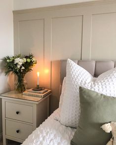 a bed with white sheets and pillows next to a night stand with flowers on it