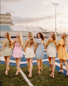 four beautiful young women standing on top of a football field holding hands and looking at the camera