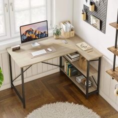 a desk with a computer on it in front of a window and bookshelf