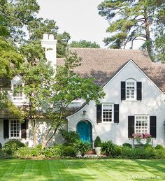 a white house with black shutters and blue door in the front yard is surrounded by lush green grass