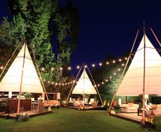 several tents are set up in the grass with lights strung from them and some chairs