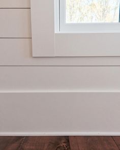 a cat sitting on the floor in front of a window with white siding and wood floors