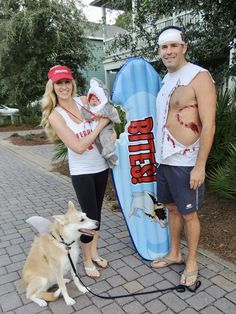 a man and woman standing next to a surfboard with a dog on a leash