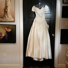 a wedding dress hanging on a door in front of pictures and an open black door