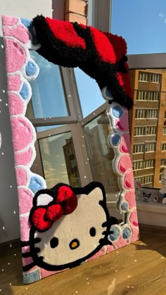 a hello kitty mirror is on the floor next to a window with a building in the background