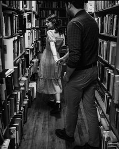 a man and woman standing in front of a bookshelf full of bookcases