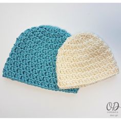 two crocheted hats sitting next to each other on a white surface, one blue and the other beige