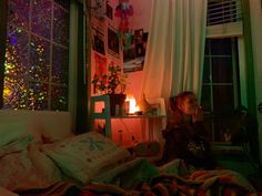 a woman sitting on a bed in front of a window with christmas lights all over it