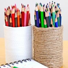 several different colored pencils are in a white container next to a notebook and pen