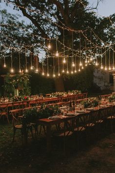 an outdoor dinner table set up with lights strung from the trees