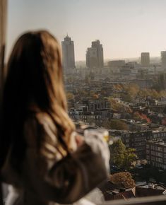 a woman looking out over a city from a high rise apartment building in the fall