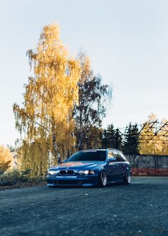 a blue car parked on the side of a road next to a tree with yellow leaves