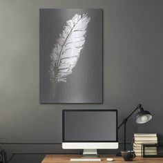 a desk with a computer, books and a lamp on it in front of a gray wall