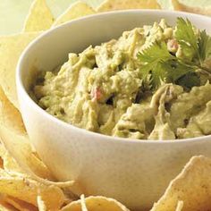 a white bowl filled with guacamole surrounded by tortilla chips