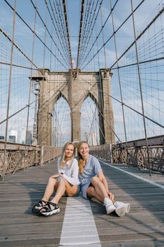 two women sitting on the ground in front of a bridge