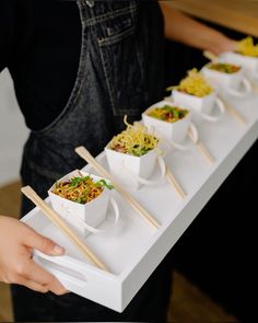 a person holding a tray with food on it and chopsticks sticking out of it