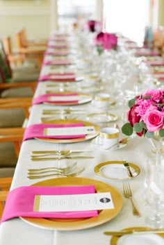 the table is set with gold and pink place settings, silverware, and flowers