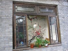 an open window with potted plants on the ledge and in between it is a brick wall