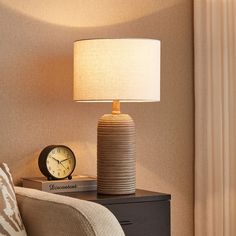 a lamp sitting on top of a night stand next to a table with a clock