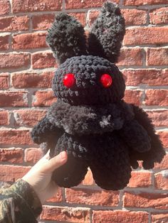 a hand holding up a black crocheted stuffed animal with red eyes and ears