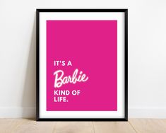 it's a barbie kind of life poster in black frame on wooden floor next to wall