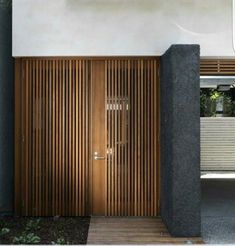 a wooden door in front of a white wall and some plants on the side walk