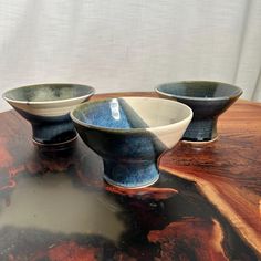 three bowls sitting on top of a wooden table with white and blue glazes