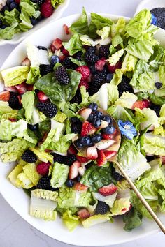 a salad with berries, blueberries and other fruits in it on a white plate