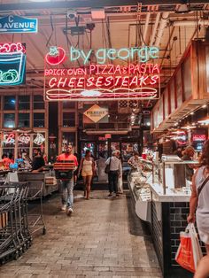 people are walking through an open market with neon signs on the walls and food carts