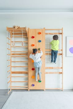 two children are climbing on the wall in an indoor climbing area with ladders and ropes