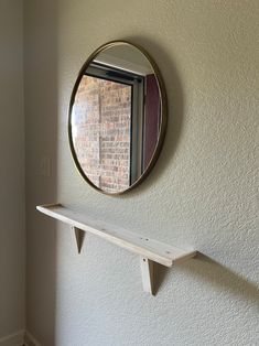 a mirror hanging on the wall above a shelf with a shelf below it and a brick wall behind it