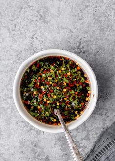 a white bowl filled with vegetables on top of a gray counter next to a spoon