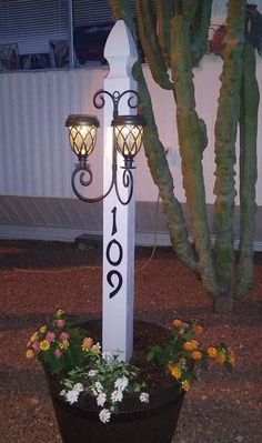 a white pole with two lights on it next to a planter and a fence