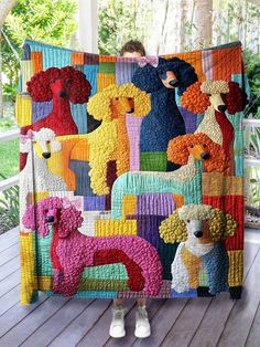 a woman holding up a colorful quilt with poodles on it