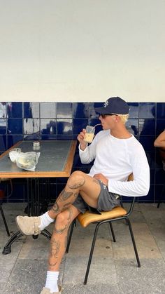 a man sitting at a table drinking from a glass in front of his face with tattoos on his legs