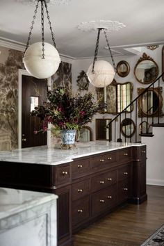 a kitchen island with marble counter tops and hanging lights above it, along with mirrors on the wall